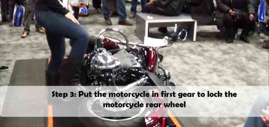 Put the motorcycle in first gear to lock the rear wheel